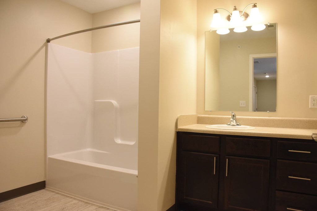 A bathroom with a white tub and brown cabinets.
