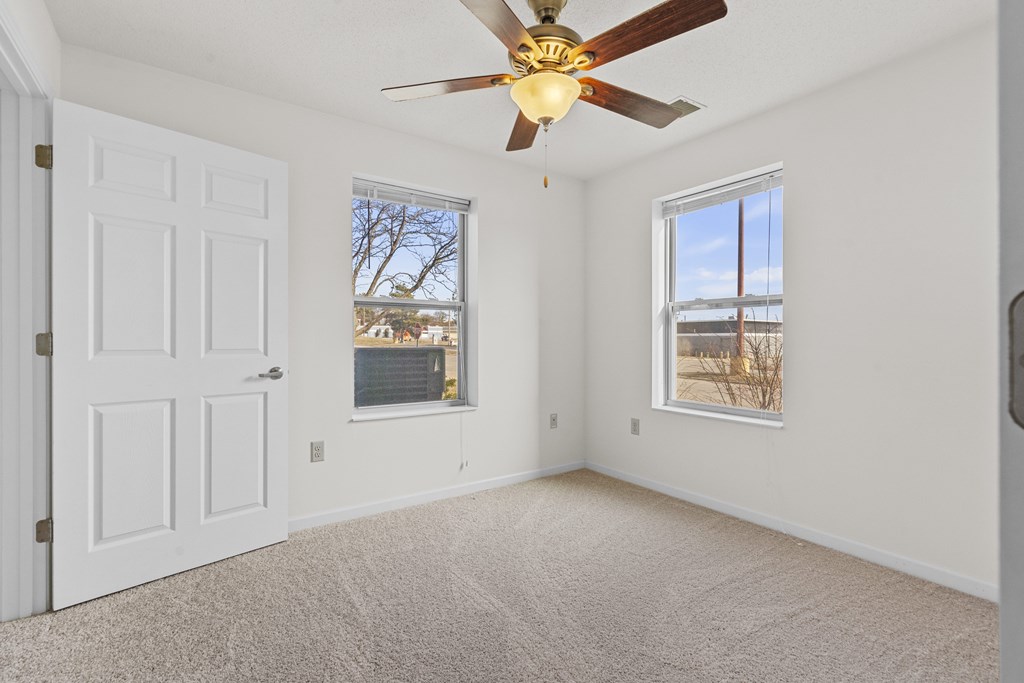 A room with a ceiling fan and two windows.