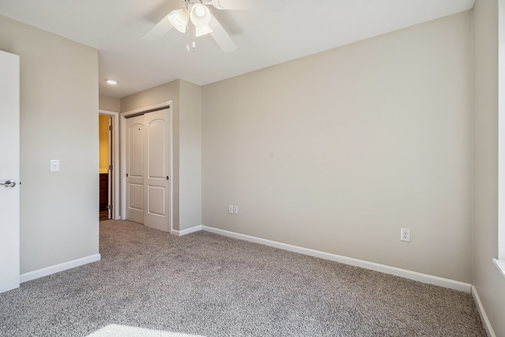 A room with a carpeted floor and a ceiling fan.