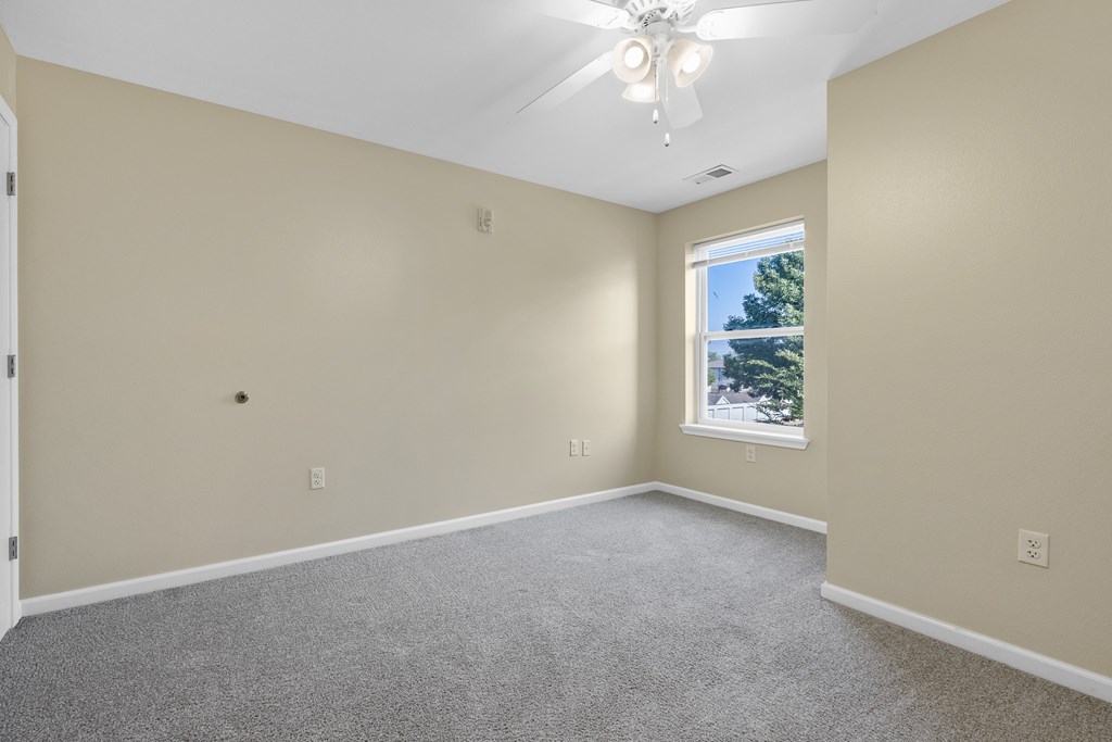 A room with a ceiling fan and a window showing trees outside.