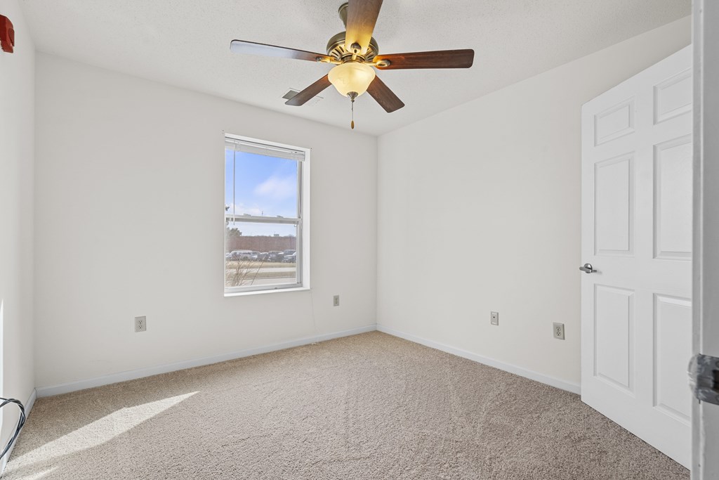 A room with a ceiling fan and a window overlooking a cityscape.