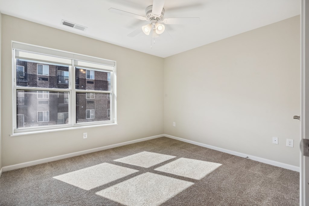 A room with a ceiling fan and a window overlooking a building.