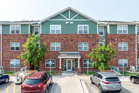 A red car is parked in front of a brick building with a green awning.
