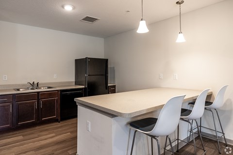 A kitchen with a black refrigerator and white chairs.
