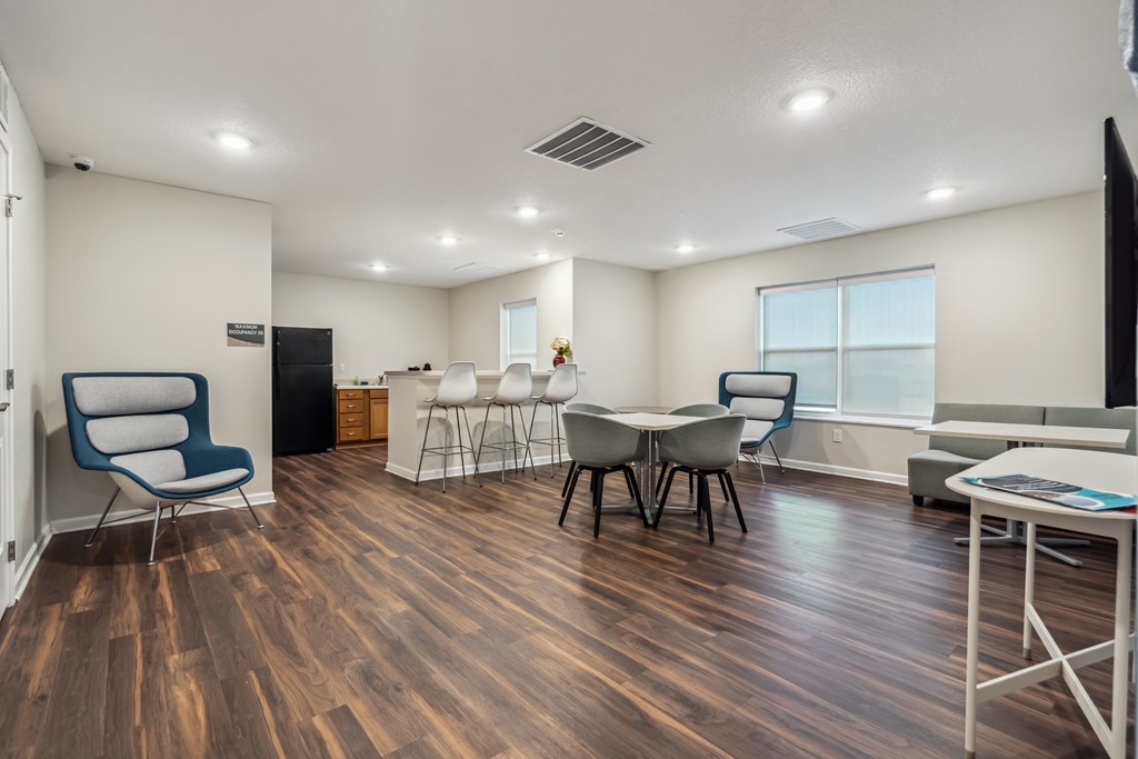 A room with a wooden floor and white walls has a table and chairs.
