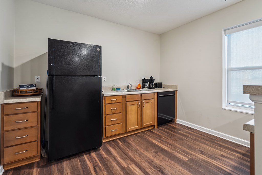 A black refrigerator sits in a kitchen with wooden floors and cabinets.