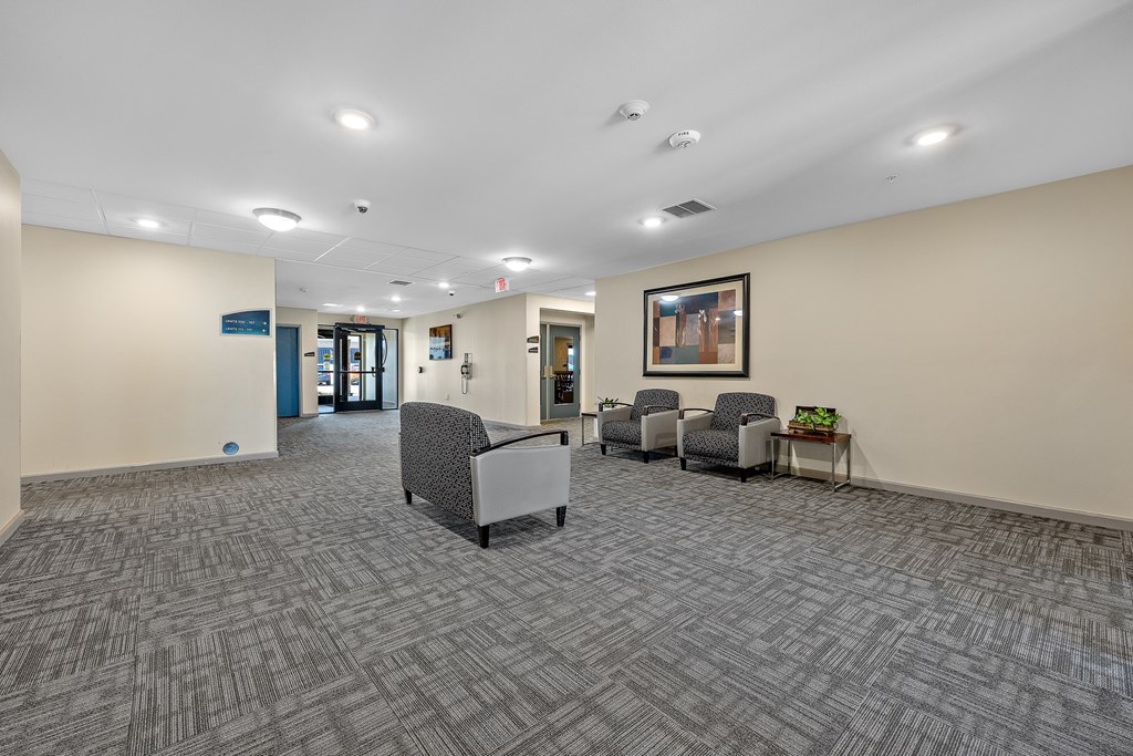 A hallway with a carpeted floor and a few chairs and a table.