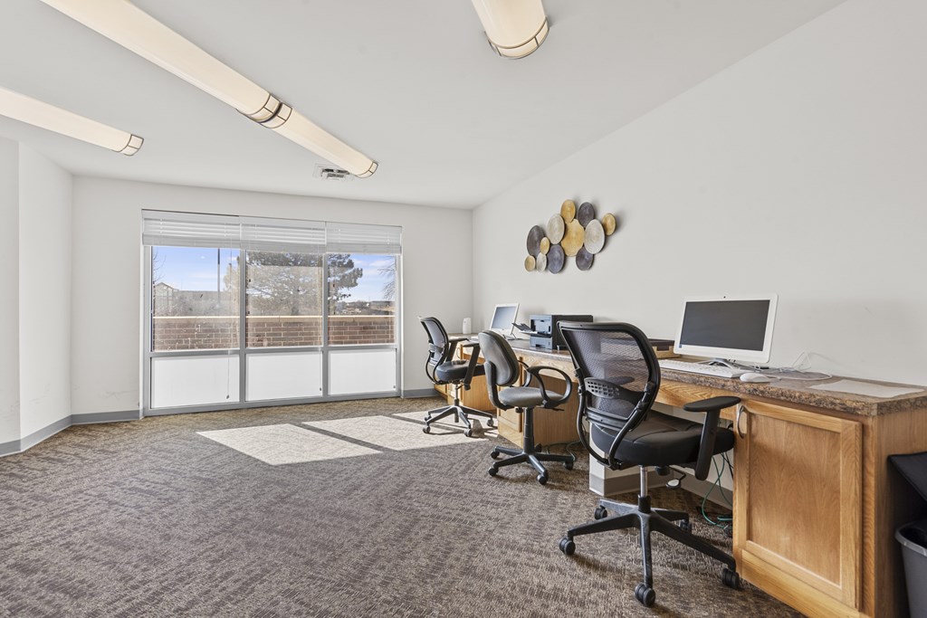 A room with a desk and chairs and a window with blinds.
