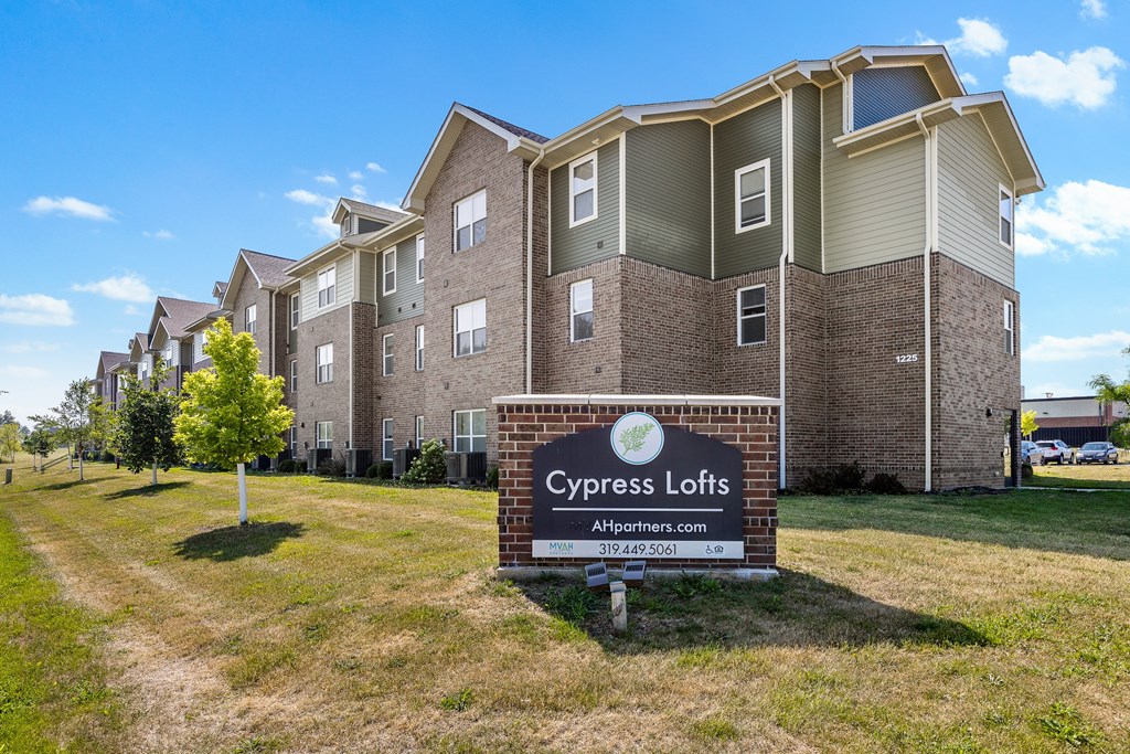 A sign for Cypress Lofts is in front of a building with a grassy area in the foreground.