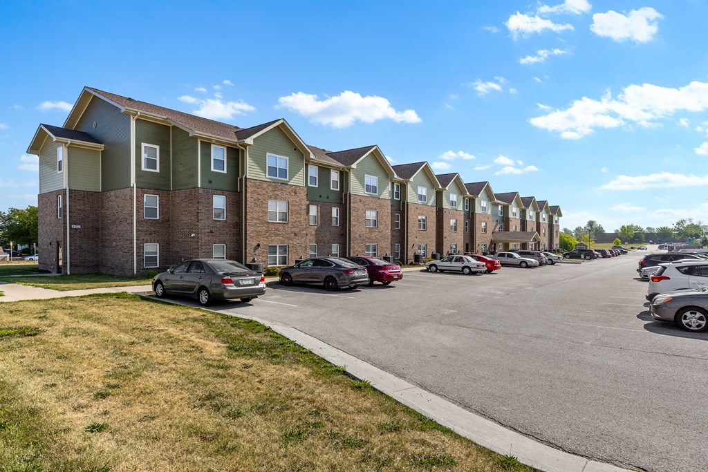 A row of apartment buildings with cars parked in front.