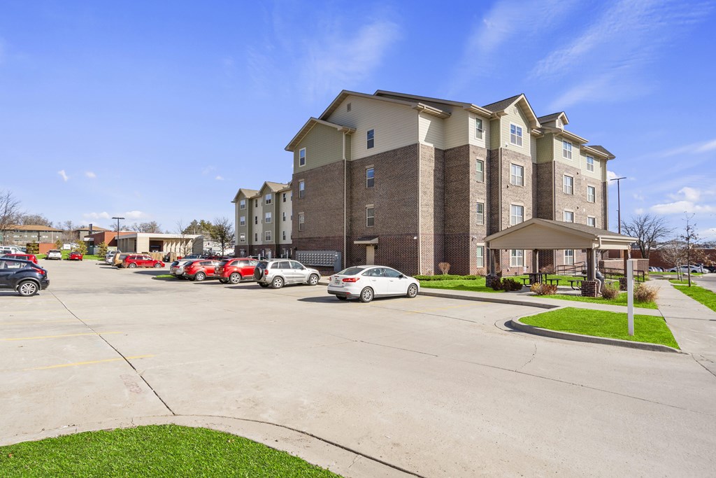 A parking lot in front of a multi-story apartment building with cars parked.