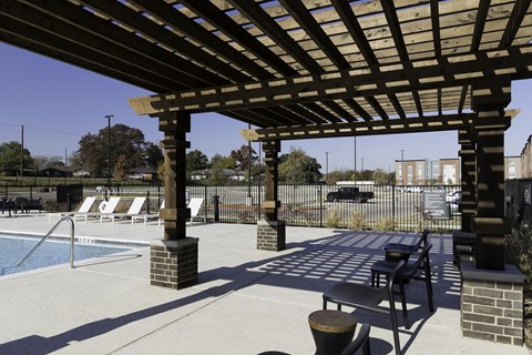 A wooden pergola over a pool with lounge chairs underneath.