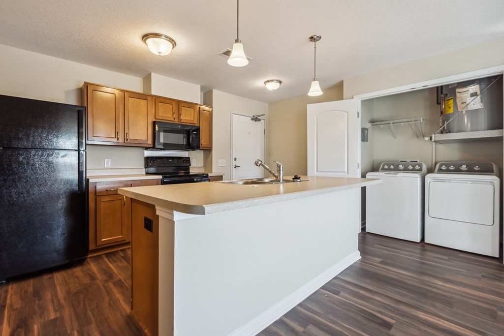 A kitchen with a black refrigerator, white countertops, and wooden cabinets.