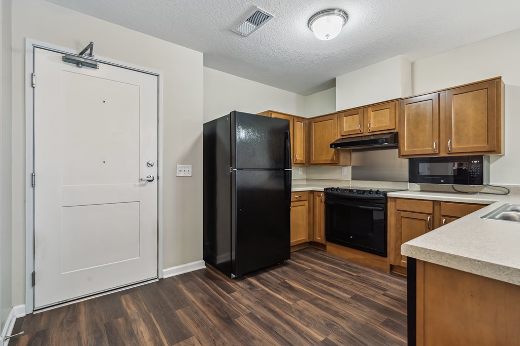 A kitchen with a black fridge and wooden floors.