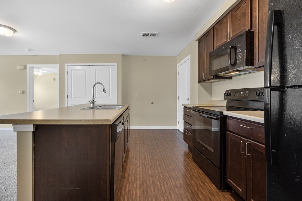 A kitchen with dark wood cabinets and a black refrigerator.