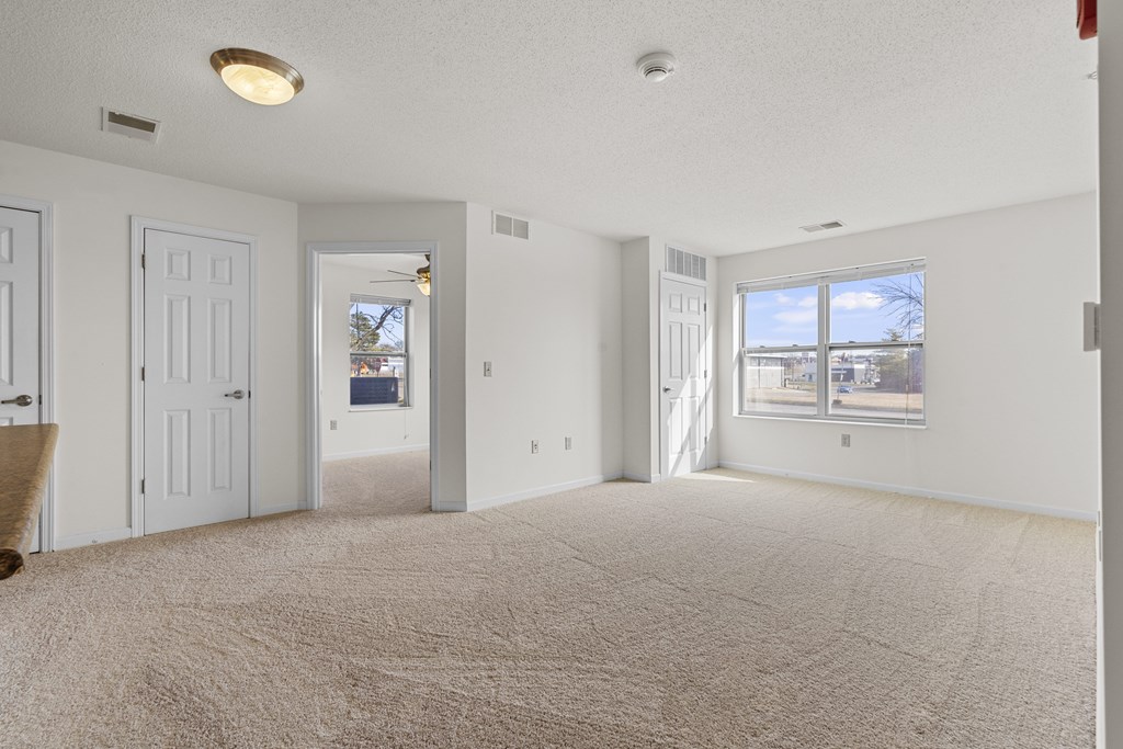 A spacious room with a carpeted floor and a window overlooking a residential area.