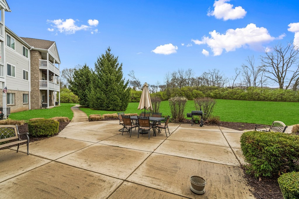 A patio with a table and chairs is surrounded by a grassy area and a building.
