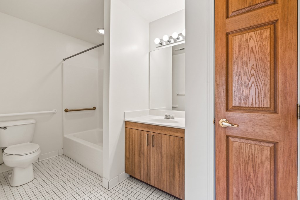 A white tiled bathroom with a wooden door.