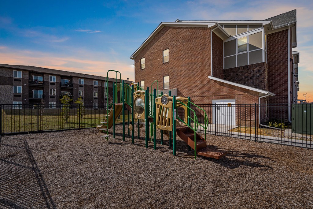 A playground with a slide and a green fence in front of a brick building.