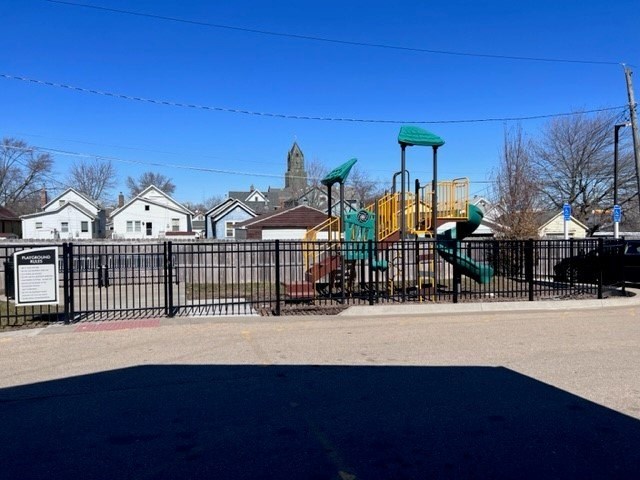 A playground with a green slide and a sign in front of a house.