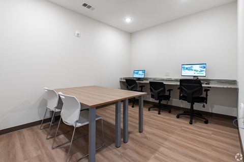 A room with a desk, chairs, and two computer monitors.