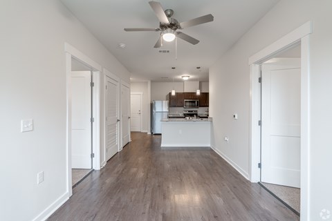 A long, empty hallway with a ceiling fan and a kitchen area visible in the distance.