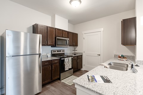 A kitchen with a refrigerator, microwave, oven, sink, and cabinets.