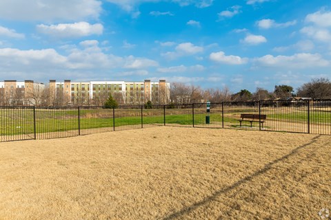A park with a bench and a fence in the foreground and a building in the background.