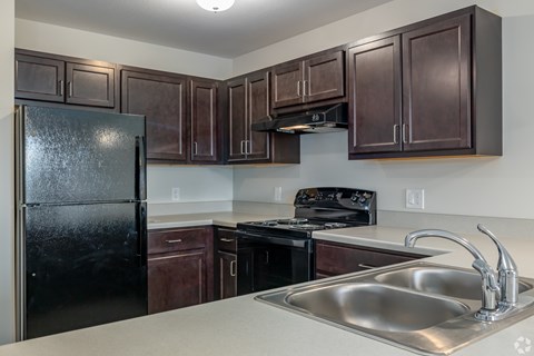 A kitchen with a black refrigerator and brown cabinets.