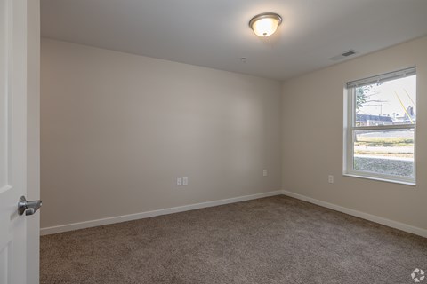 A room with a carpeted floor, a window, and a door.