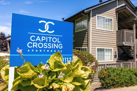 A blue sign for Capitol Crossing Apartments stands in front of a building.