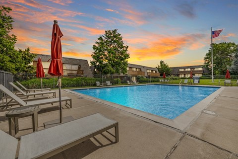 A pool with sun loungers and umbrellas is surrounded by a building.