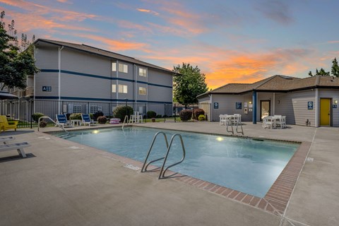 A pool area with a diving board and lounge chairs in front of a building.