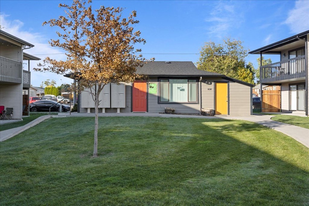 Leasing office exterior with large windows and an orange and yellow door. Green grass and a tree in front, and a parking lot behind the building. at Brix, Walla Walla, WA, 99362
