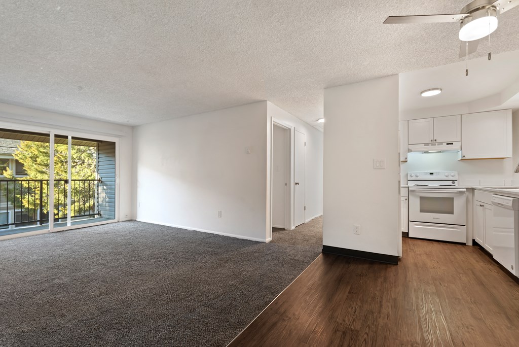 the living room and kitchen of an apartment with white appliances and wood flooring