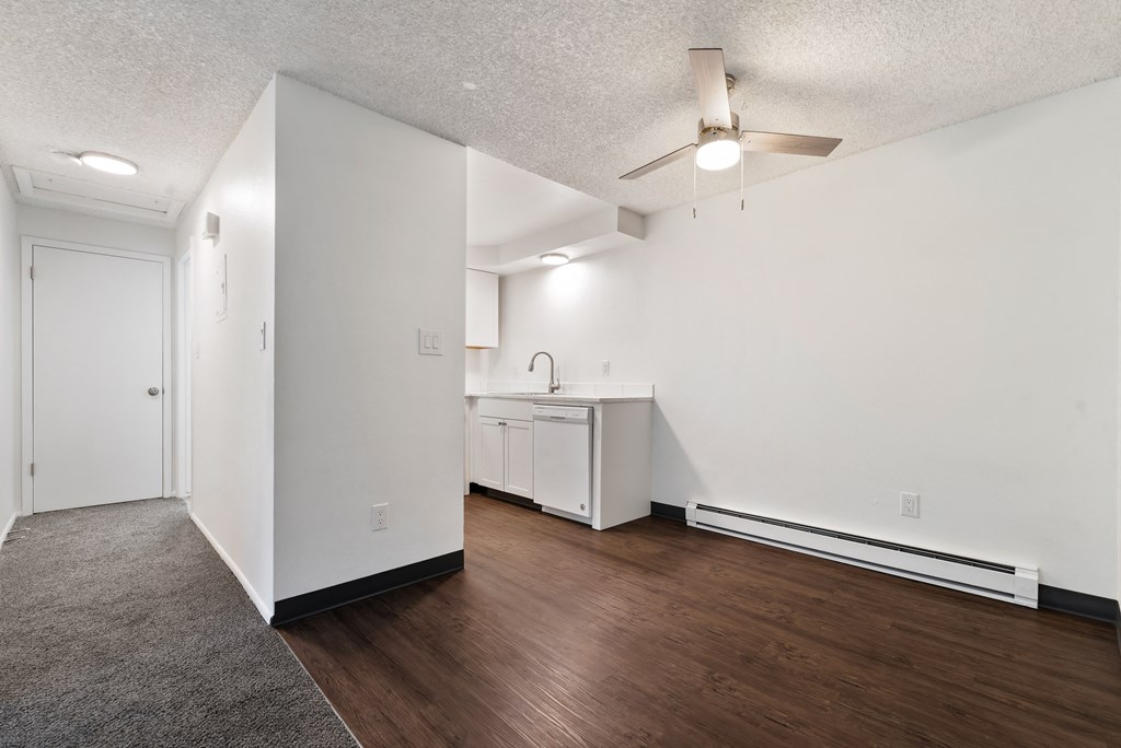an empty living room and kitchen with white walls and wood flooring