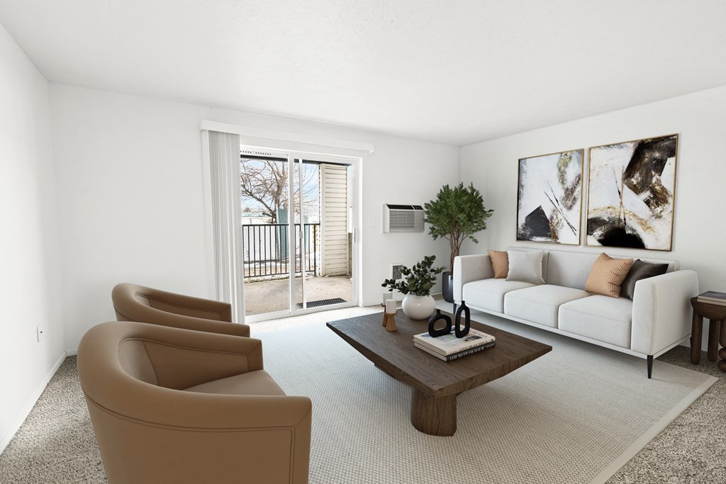 A bright living room with white walls and two glass sliding doors to a private balcony. Staged with a couch, 2 chairs, table and plant.at North Pointe, Post Falls, 83854