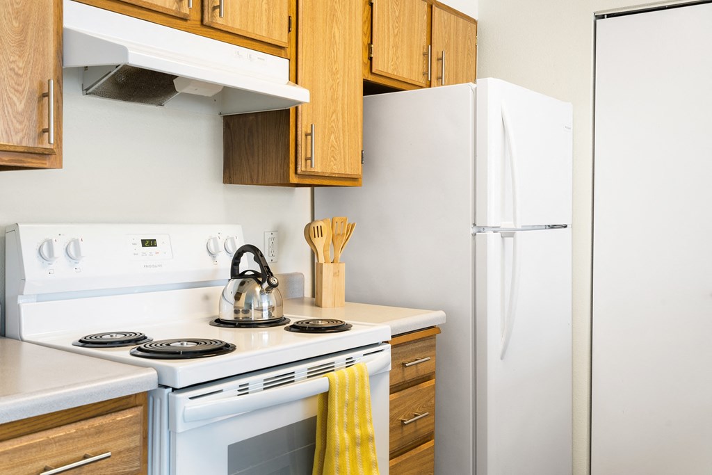 The corner of the kitchen with a white oven, stove top, hood range, and full-size fridge. Staged with a tea kettle, wooden spoons, and a hand towel.at Clearwater, Post Falls
