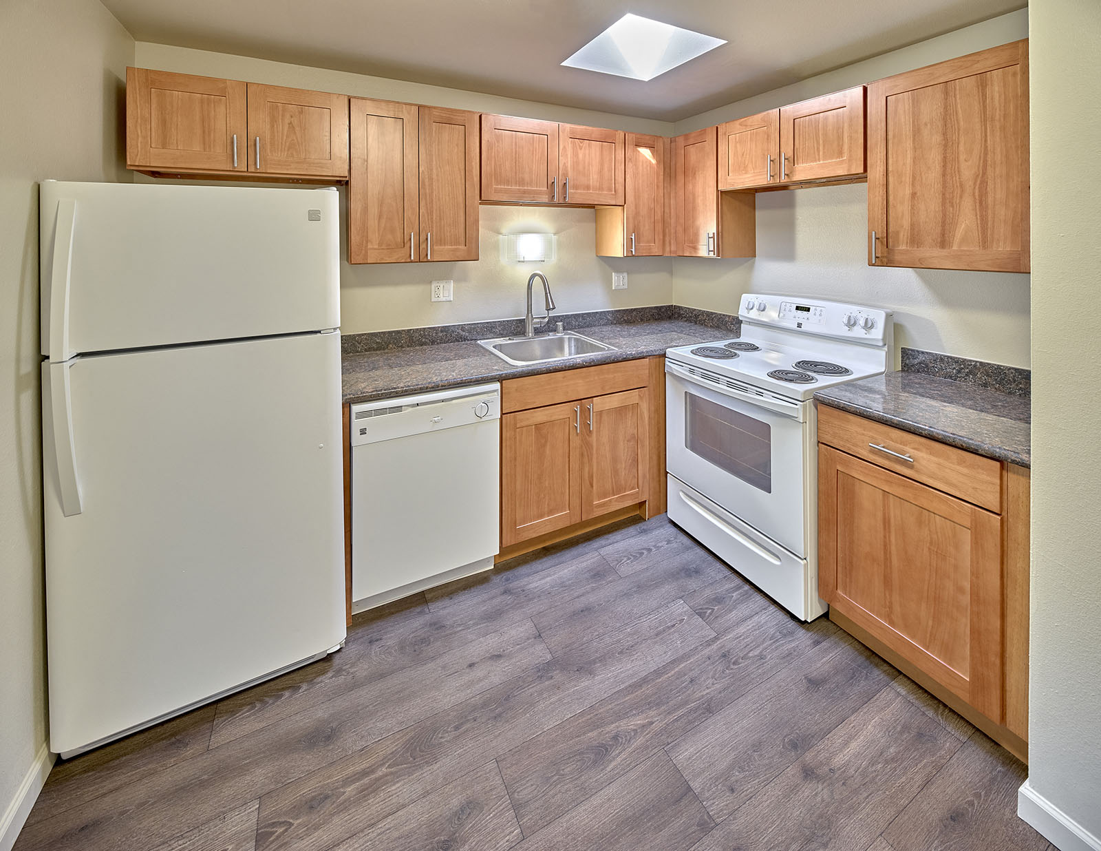 L shaped kitchen with white appliances, light brown cabinets and wood style flooring.at Park View Apartments, Wenatchee