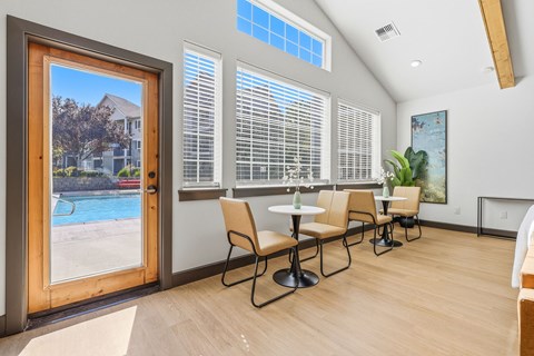 A room with a table and chairs and a view of a pool through a glass door.
