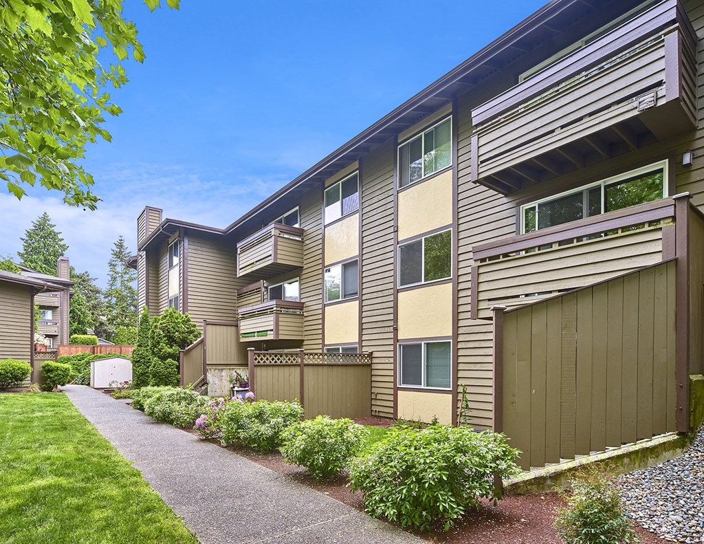 Exterior view of personal patios or balconies, manicured grounds and building, and blue skies in the background at Heritage Grove, Renton, WA.
