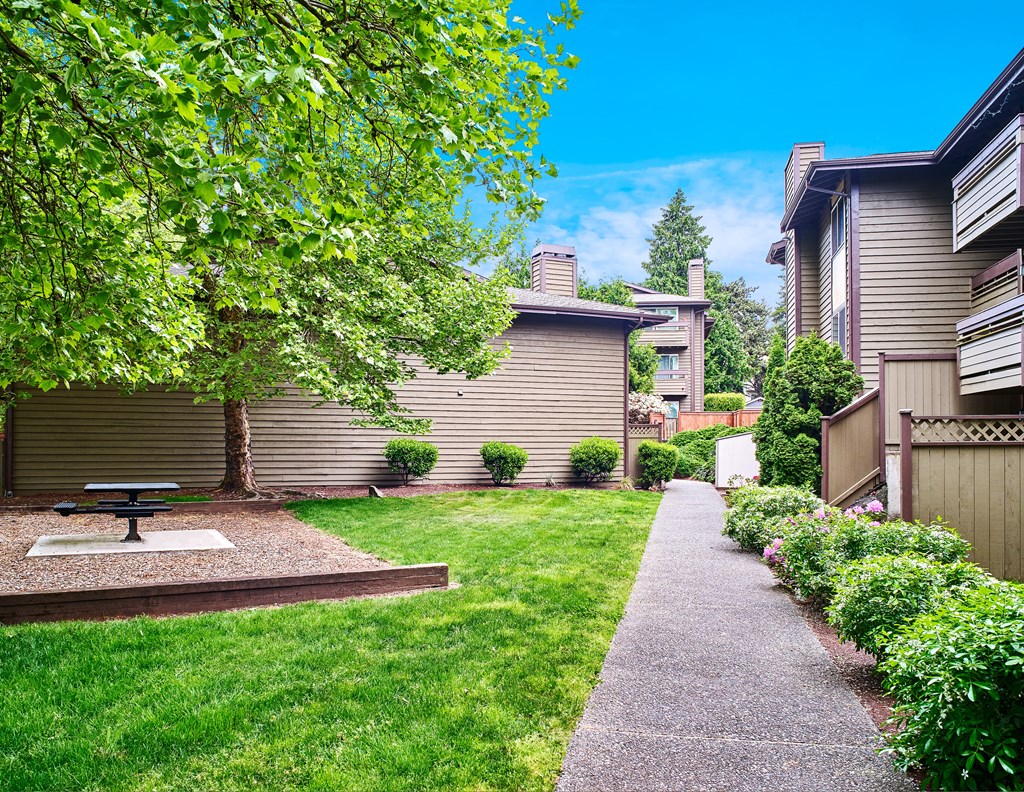 A backyard with a picnic table and a concrete path at apartments in Renton, WA.