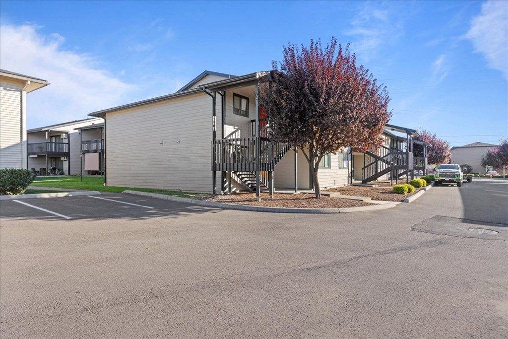 The corner of an apartment building with a red tree and landscaping around. Community parking is to the left. at Brix, Walla Walla, WA, 99362