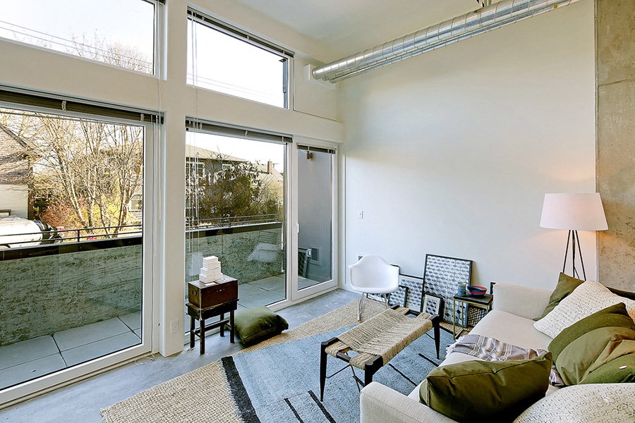 Living room with concrete flooring, floor to ceiling windows and a private outdoor patio. Inside is staged with a coffee table, rug and chair.at 19th & Mercer, Washington
