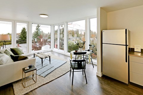 Living room with floor to ceiling windows with city and tree views. Staged with a couch, coffee table, rug and chair.at 19th & Mercer, Seattle Washington