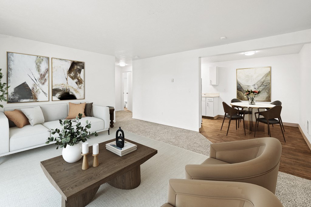 A bright living room with taupe carpets, white walls and staged with a white couch, a coffee table, two chairs and wall art.at North Pointe, Post Falls, ID