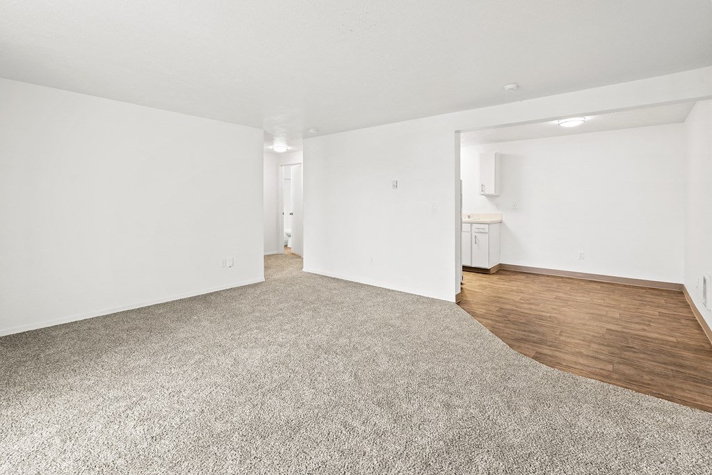 Bright white living room area with taupe carpet, and view of dining area with faux wood flooring at the far right back of the photo.at North Pointe, Post Falls, ID