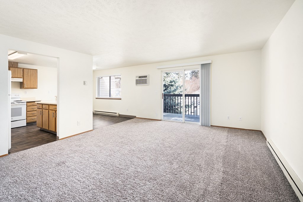 A carpeted living room with sunny windows looking out to the kitchen, dining area, and private balcony.at Clearwater, Idaho
