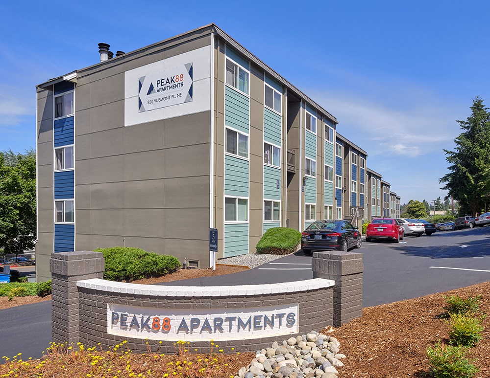 Community entrance with orange and gray 'Peak 88' sign surrounded by flowers and landscaping.