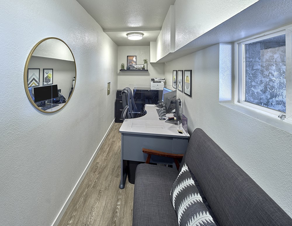Leasing office with a couch, chair, desk, mirror, and window on the right wall.